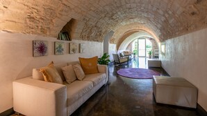 A cozy interior with a stone ceiling, a sofa with cushions, a round table, and a chair.
