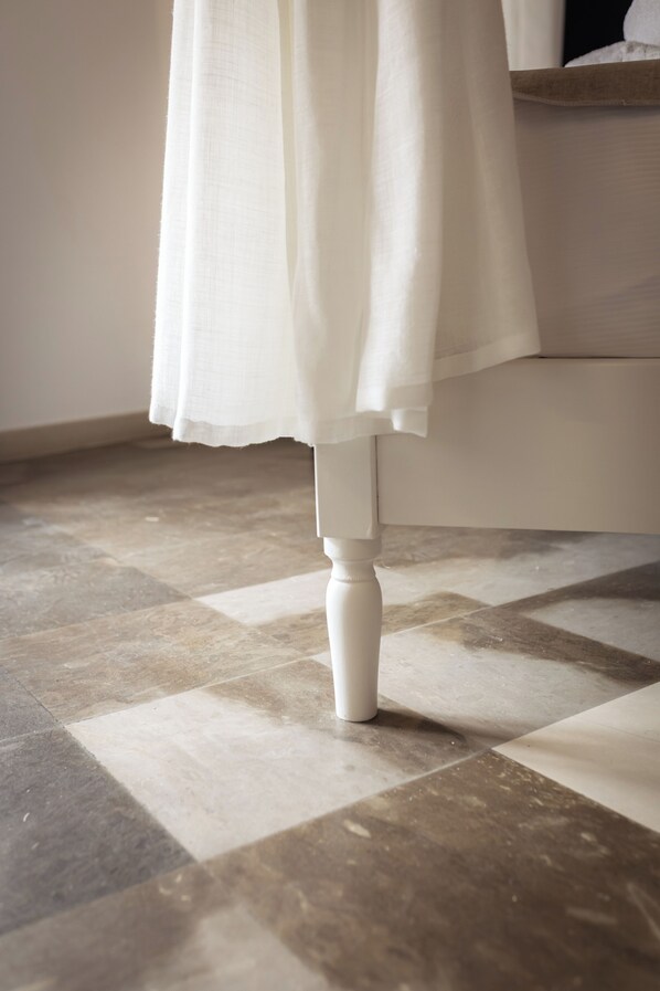 Un baño con piso de baldosas, una cortina blanca y un lavamanos pedestal blanco.