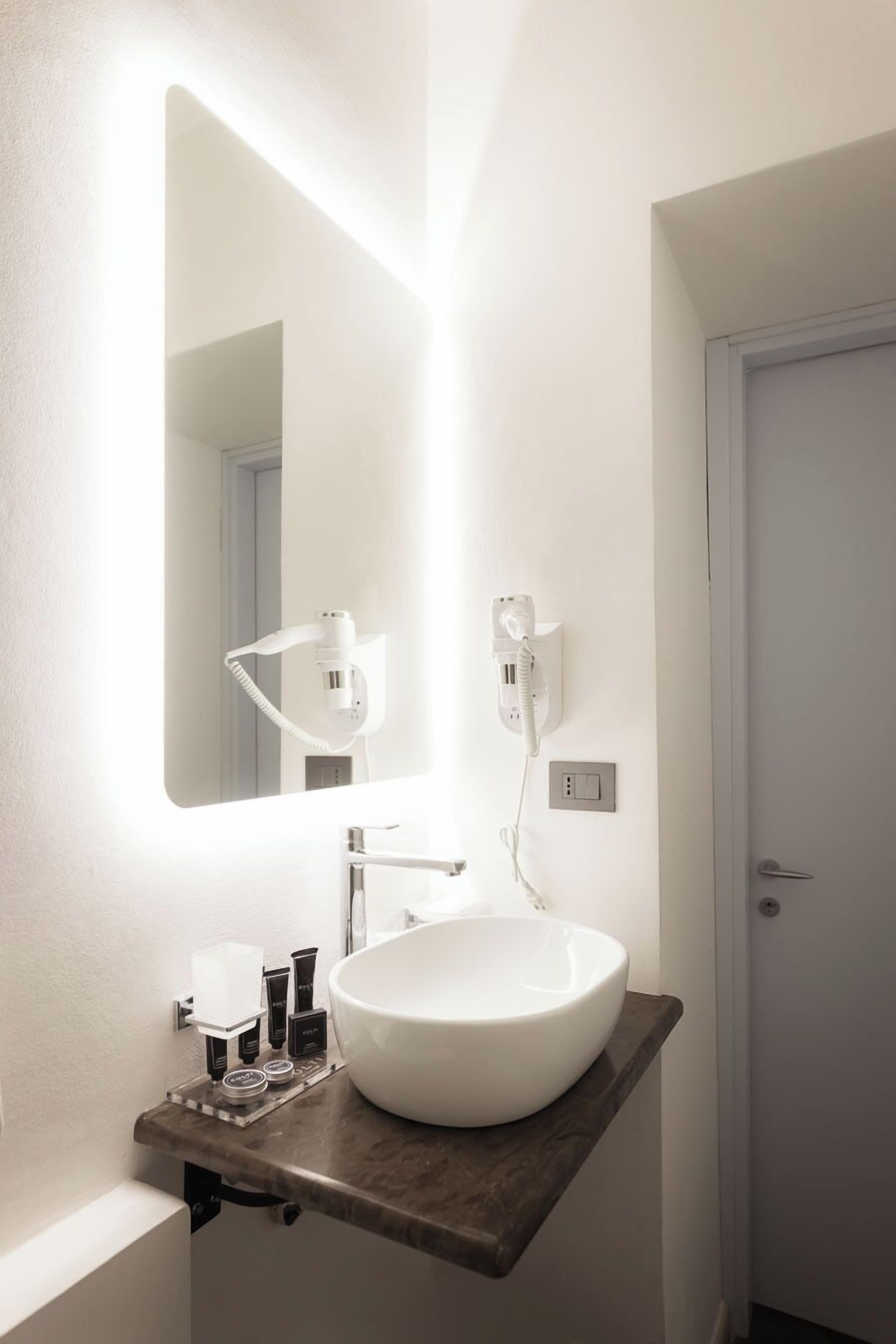 Un baño con un lavamanos blanco, un espejo grande y un secador de pelo en la pared.