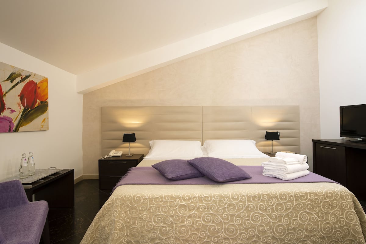 Une chambre d’hôtel avec un lit, deux tables de chevet, une télévision, un tableau et une chaise.