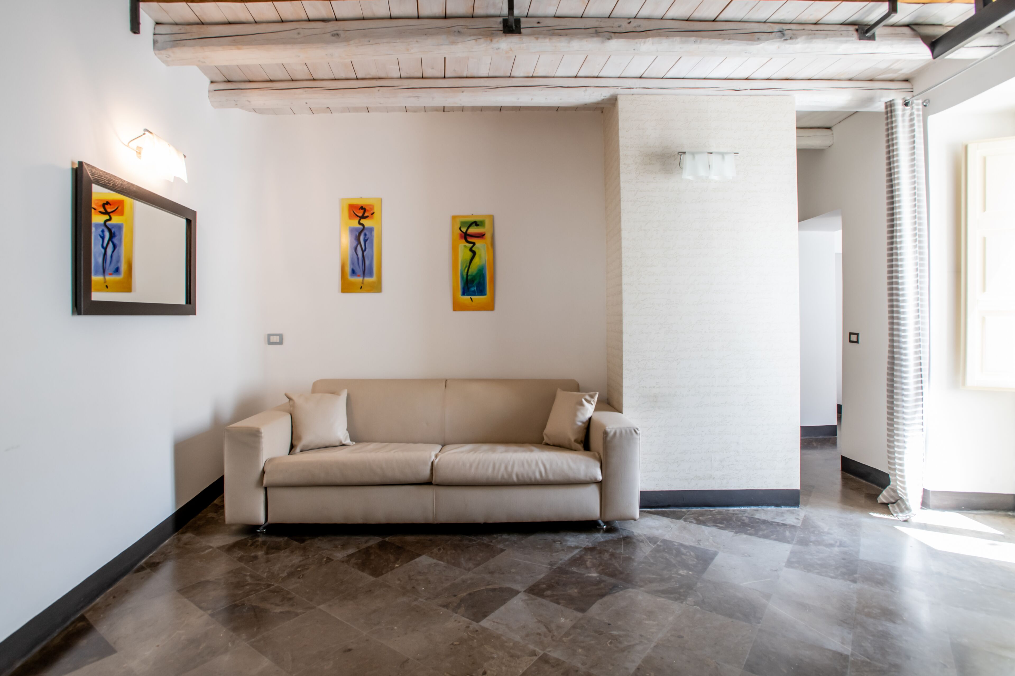 A modern living room with a beige sofa, a tiled floor, and abstract art on the wall.