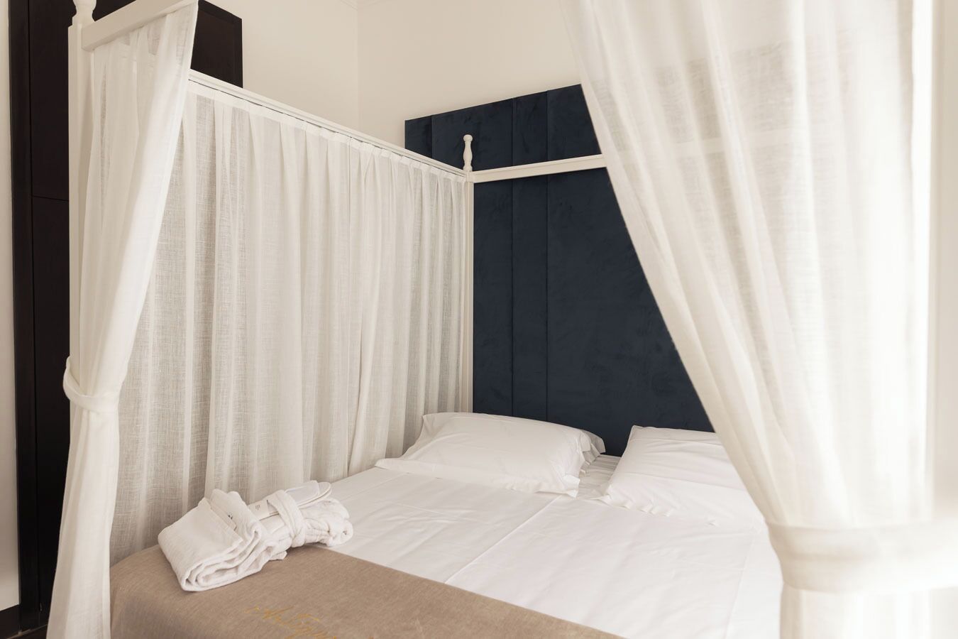 Una cama con sábanas blancas, una toalla enrollada y un dosel.