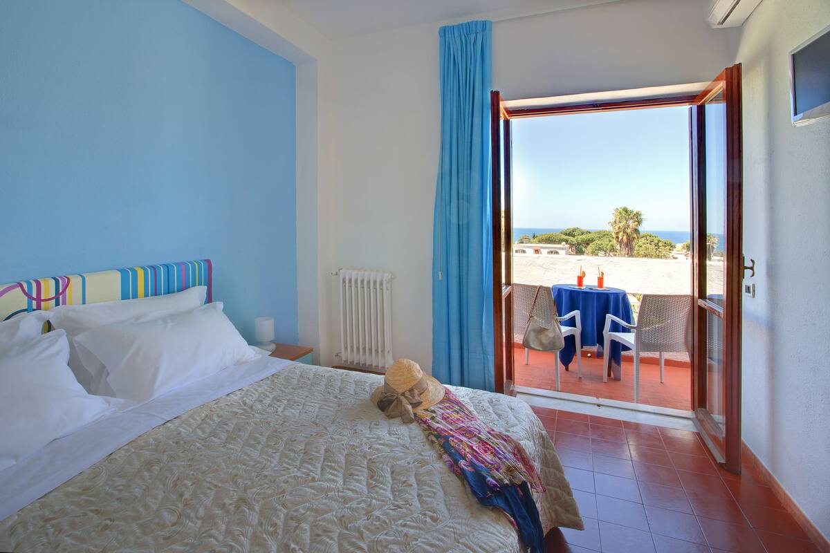 A hotel room with a bed, a view of the beach, and a balcony with a table and chairs.