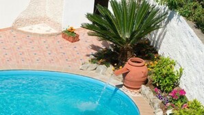 Eine Frau liest ein Buch am Pool mit einer Fliesenveranda und einer Steinmauer.