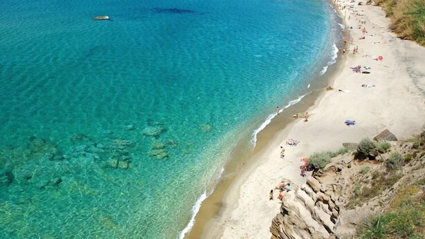 Ein Strand mit klarem türkisblauem Wasser, Felsformationen und Menschen, die sich sonnen.