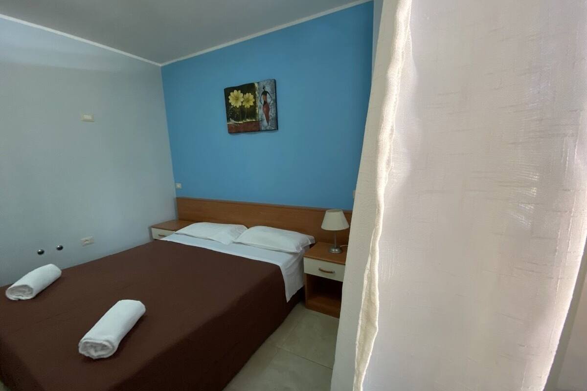 Een hotelkamer met een enkel bed, een nachtkastje, een lamp en een schilderij aan de muur.