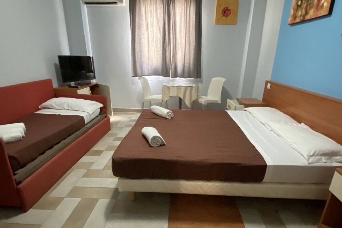 Een hotelkamer met een bed, een bank, een televisie, een klein tafeltje en stoelen.