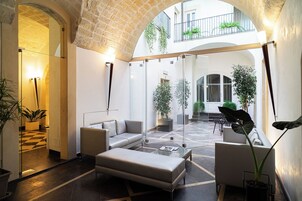 A spacious indoor area with a high ceiling, featuring a seating arrangement with a sofa and chairs, a coffee table, and potted plants.