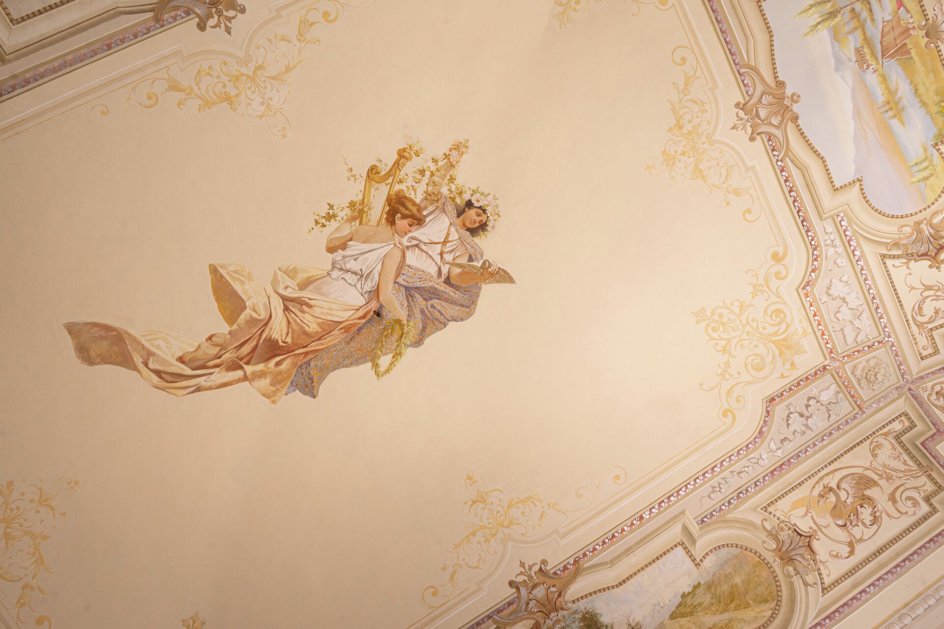 Un plafond orné de motifs dorés et surmonté d’une fresque centrale représentant une femme tenant une branche.