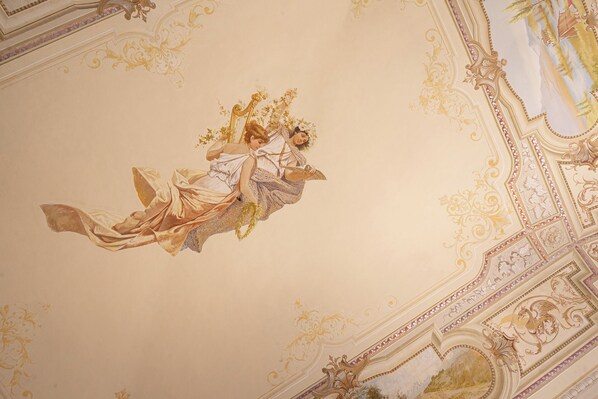 A ceiling with ornate gold detailing and a central mural of a woman holding a branch.
