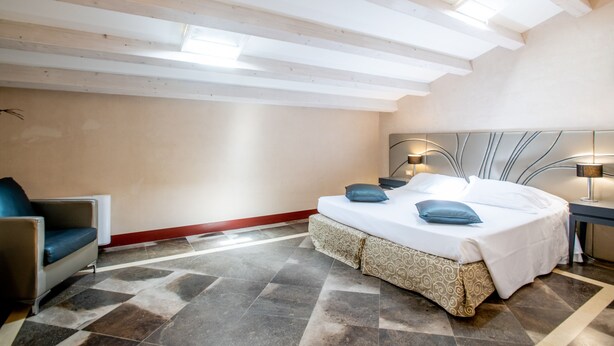 A modern bedroom with a bed, bedside table, lamp, and a chair. - De Stefano Palace (Ragusa)