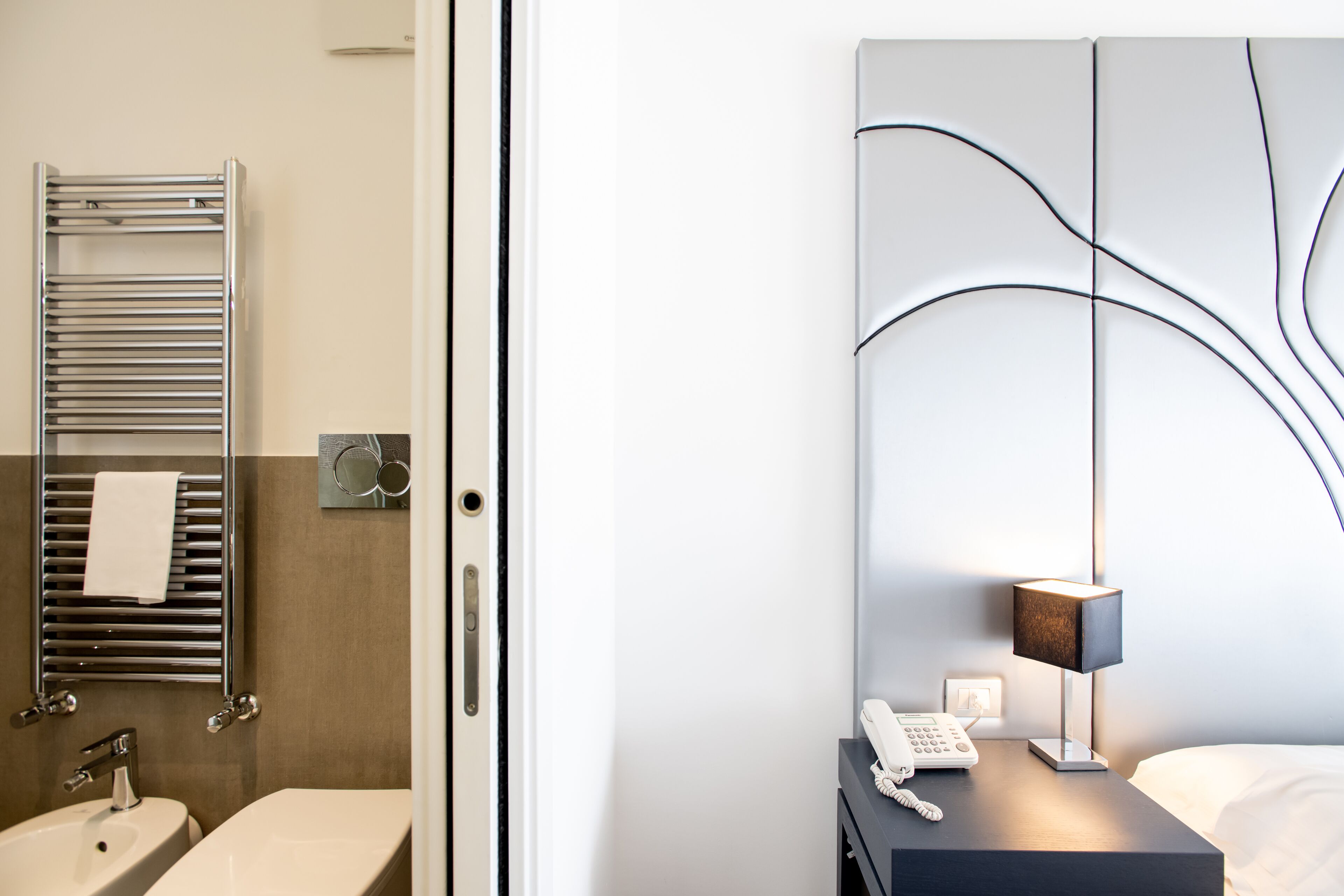 Ein modernes Badezimmer mit Handtuchhalter, Waschbecken und Toilette. Ein Nachttisch mit Lampe und Telefon ist ebenfalls vorhanden.