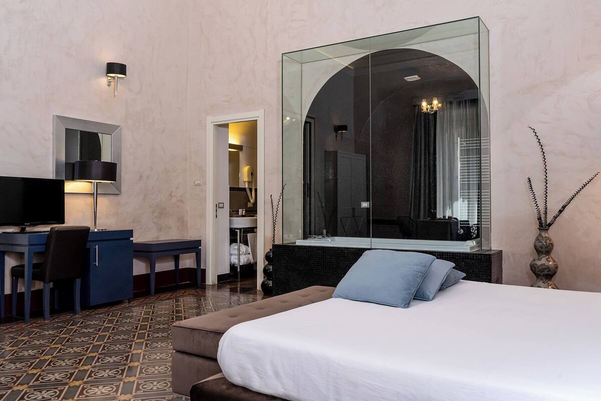 A hotel room with a bed, a desk, a chair, a television, and a large mirror.