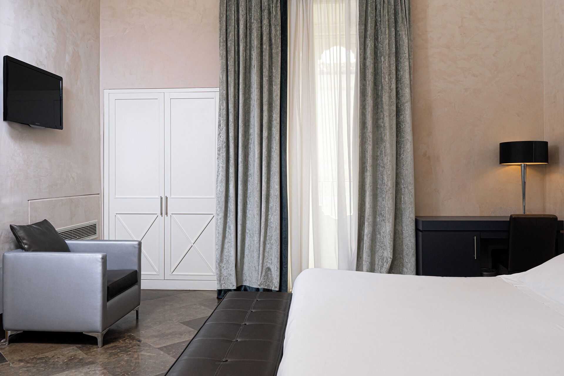 A hotel room with a bed, a sofa, a desk, a TV, and a window with curtains.