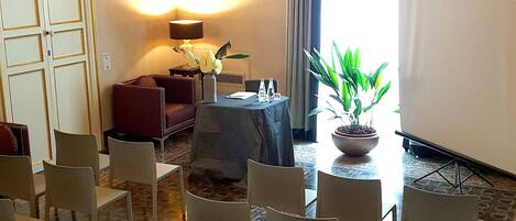 A conference room with white chairs, a table with a plant, a sofa, and a lamp.