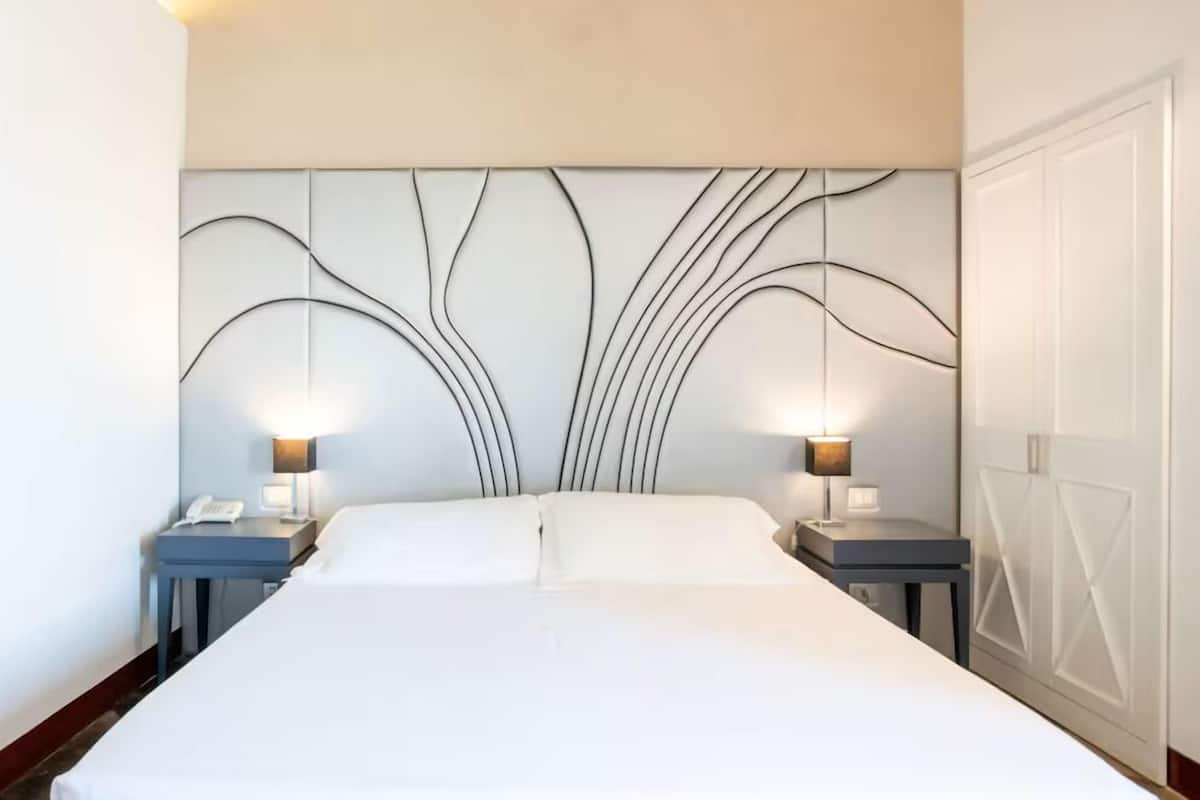 A hotel room with a large bed, two bedside tables with lamps, and a decorative wall panel.