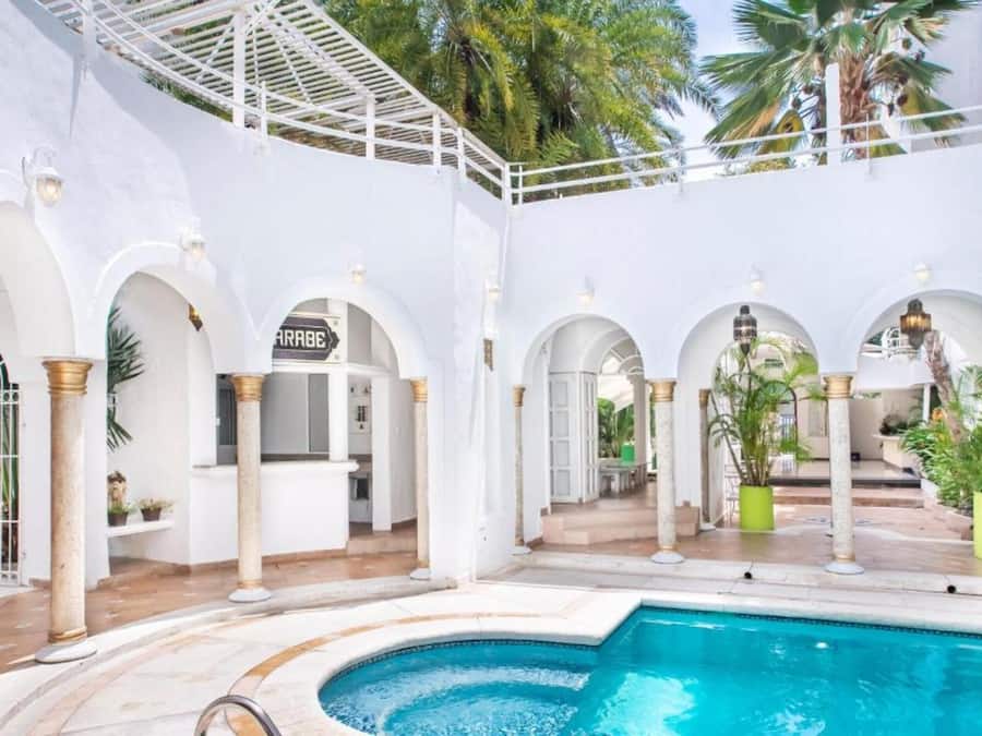 A pool area with a white exterior, arched columns, and a sign that reads "ARRA".
