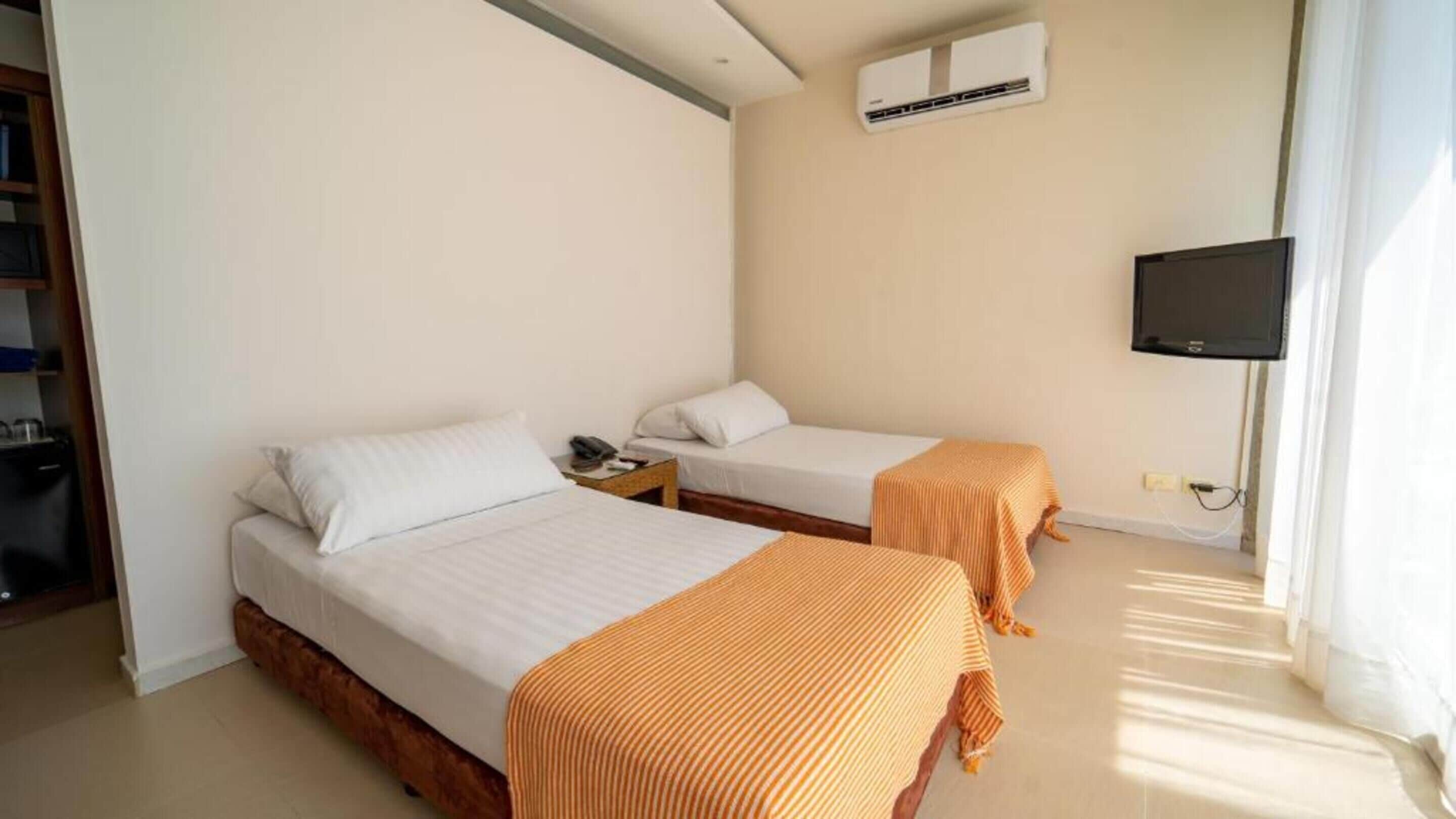 A hotel room with two beds, a TV, and an air conditioning unit.