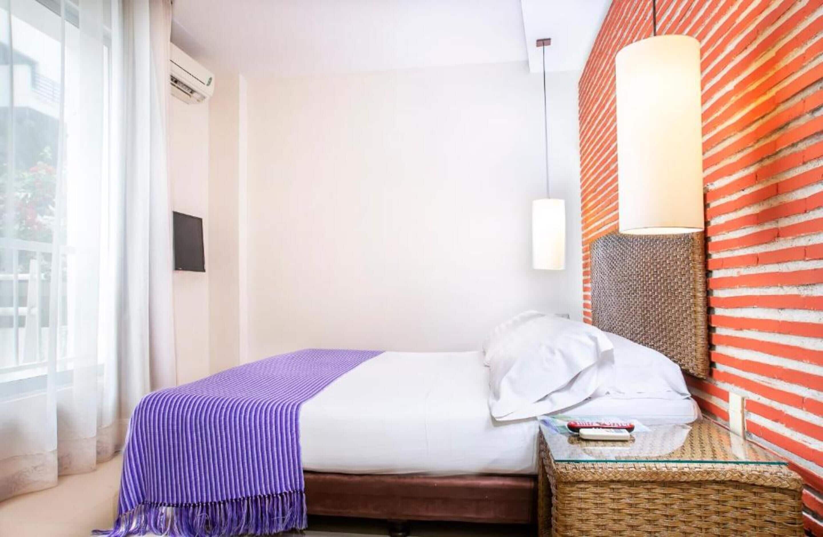 A hotel room with a bed, a nightstand, a lamp, and a window with curtains.