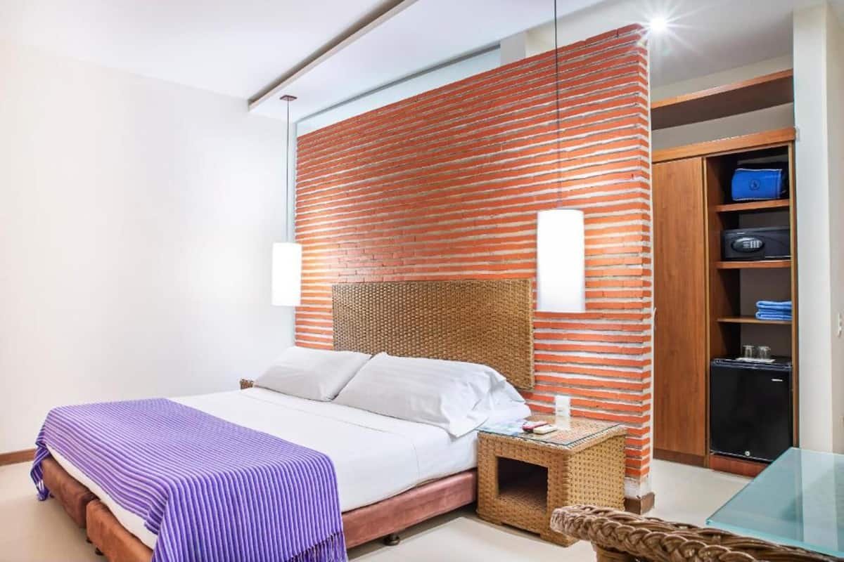 Quarto moderno com parede de tijolos, cama com roupa de cama branca, mesa de cabeceira de vime e mesa de vidro.