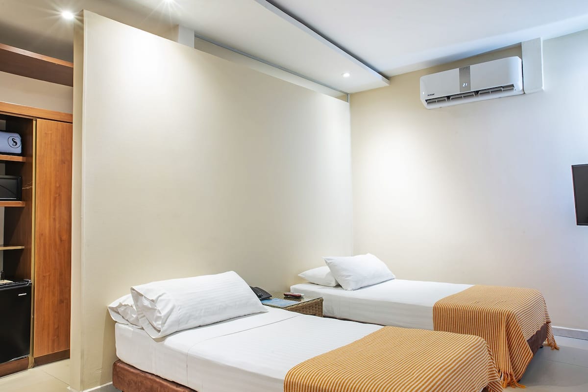 Quarto de hotel com duas camas de solteiro, um guarda-roupa, uma TV e um aparelho de ar condicionado.