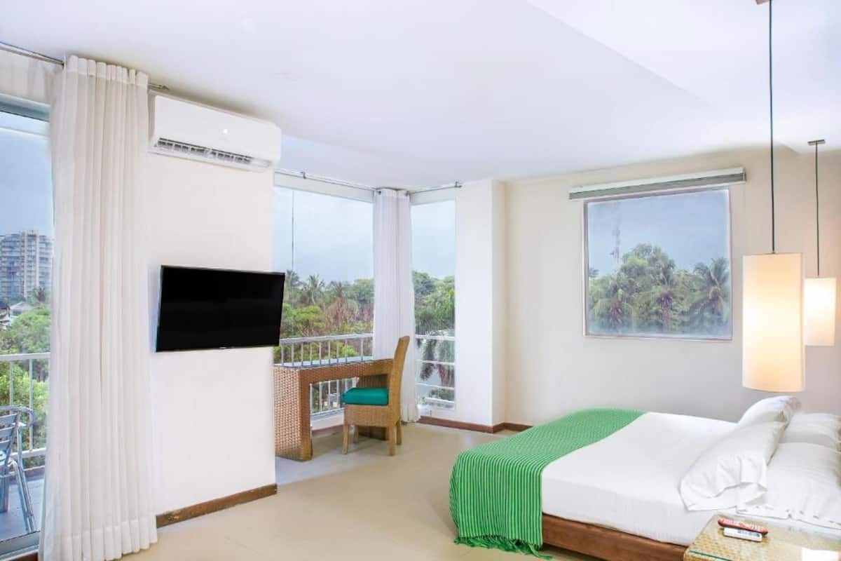 Quarto de hotel com varanda, cama, televisão e janela com vista para o verde.