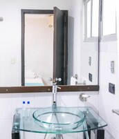 Un baño con un lavabo de vidrio, un espejo y una puerta que da a otra habitación.