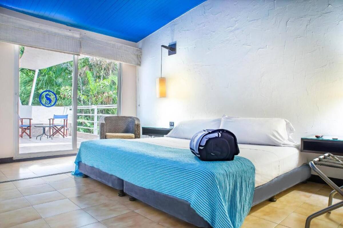 Une chambre d’hôtel avec un lit, une valise, une table de chevet et une vue sur l’extérieur.