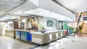 Een hotel receptie met een balie, een grote poster, een potplant en een bord met daarop een restaurant.