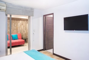 A room with a bed, a TV mounted on the wall, a sliding door leading to a balcony with a red sofa, and a stone wall.