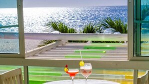 Een tafel met twee stoelen en twee drankjes op een balkon met uitzicht op een strand.