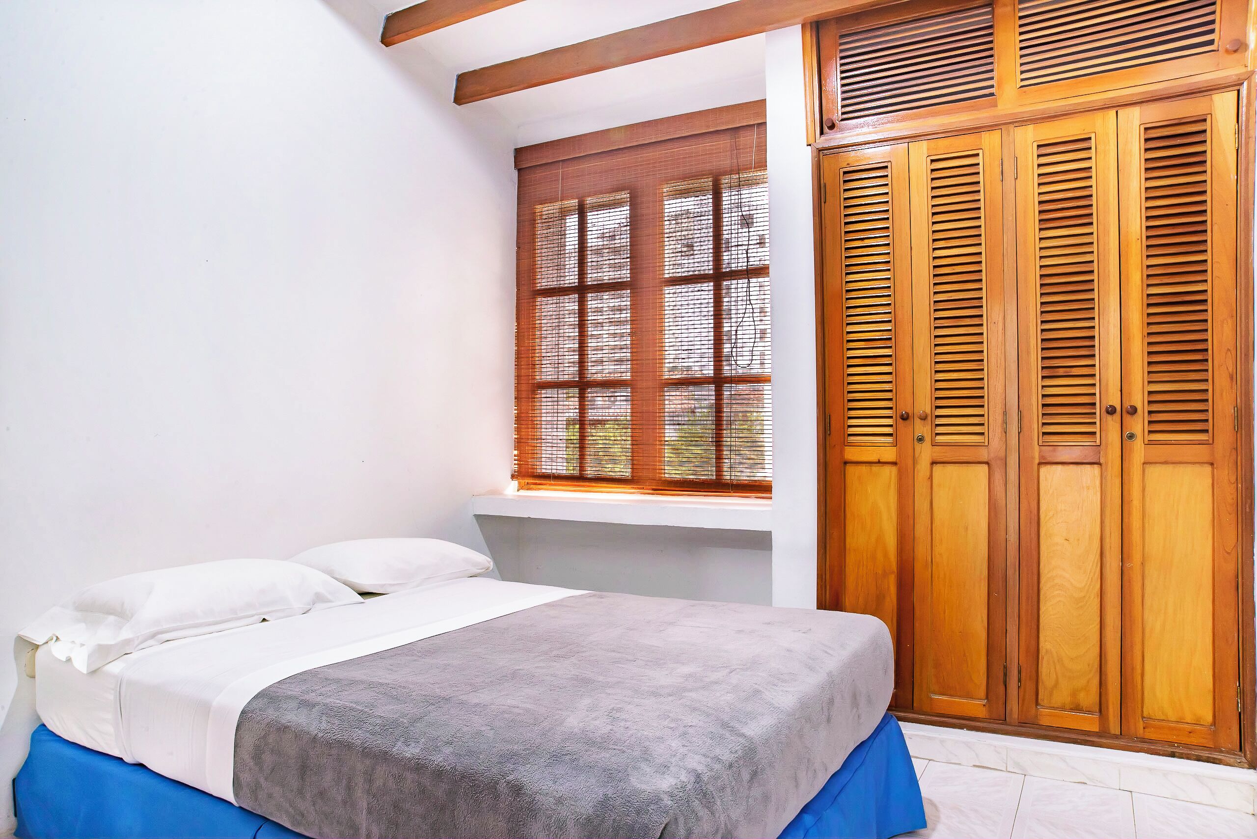 A bedroom with a bed, a window with blinds, and wooden wardrobes.