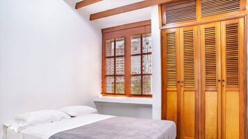 A bedroom with a bed, a window with blinds, and wooden wardrobes.