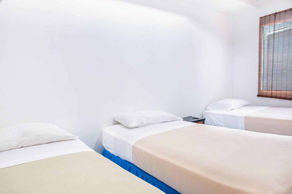 Une chambre avec deux lits, des murs blancs et une fenêtre avec des stores.