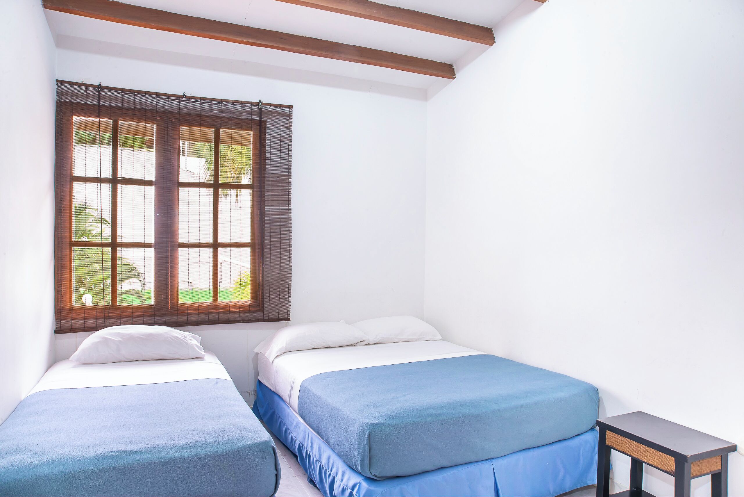 Una habitación con dos camas, una ventana con persianas y una pequeña mesa.