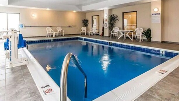An indoor swimming pool with a clear water surface, surrounded by white chairs and tables, and a no diving sign on the pool edge. - Comfort Suites South Point - Huntington (South Point)