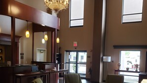 A lobby with a reception desk, green armchairs, a chandelier, and large windows. - Comfort Suites South Point - Huntington (South Point)