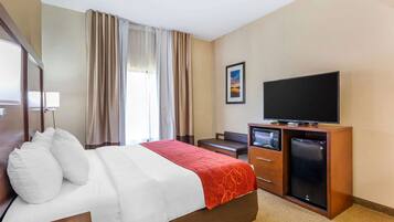 A hotel room with a bed, a television, a desk, and a refrigerator.