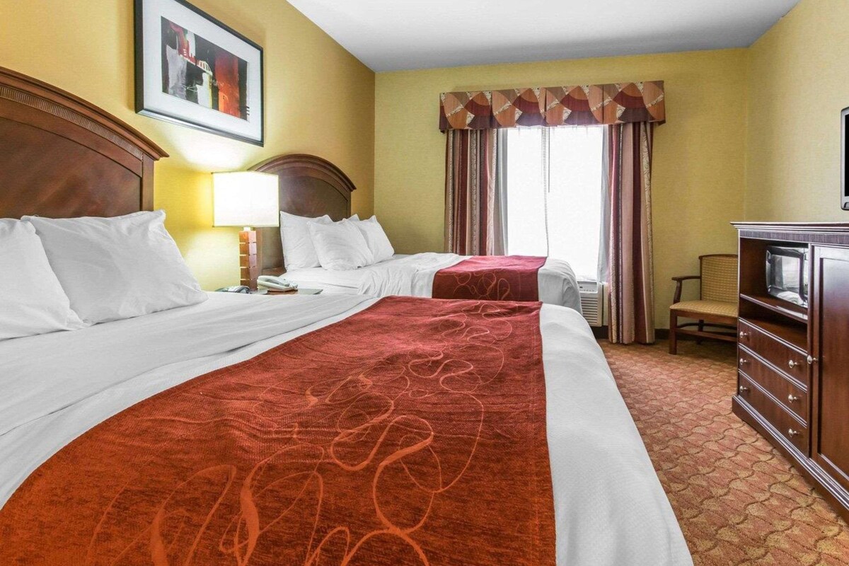 A hotel room with two beds, a desk, a chair, a TV, and a window with curtains.