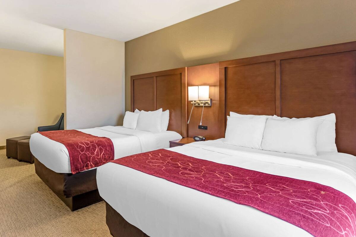 A hotel room with two beds, a wooden headboard, a nightstand, and a lamp.