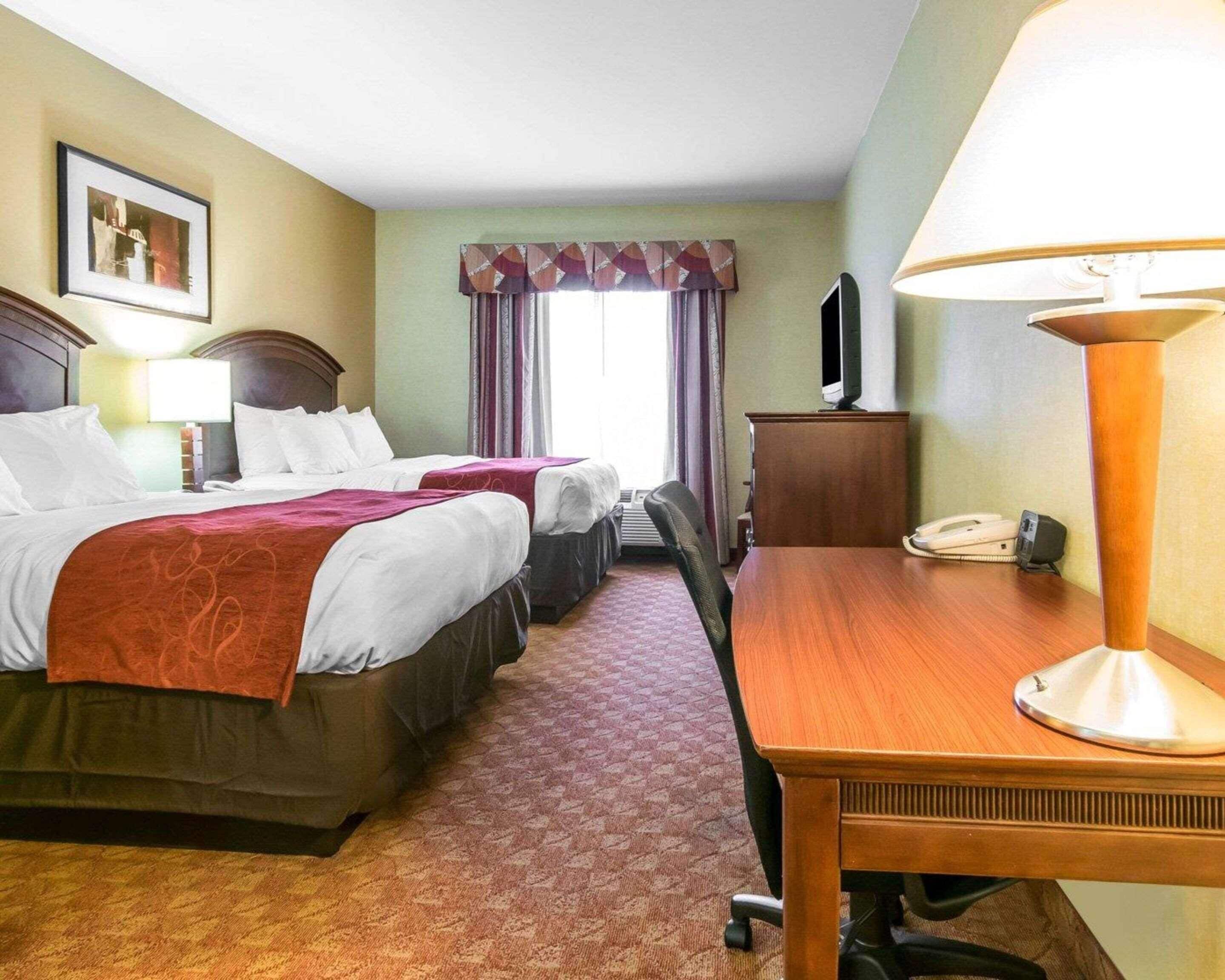 Une chambre d’hôtel avec deux lits, un bureau, une chaise, une lampe, une télévision et un téléphone.