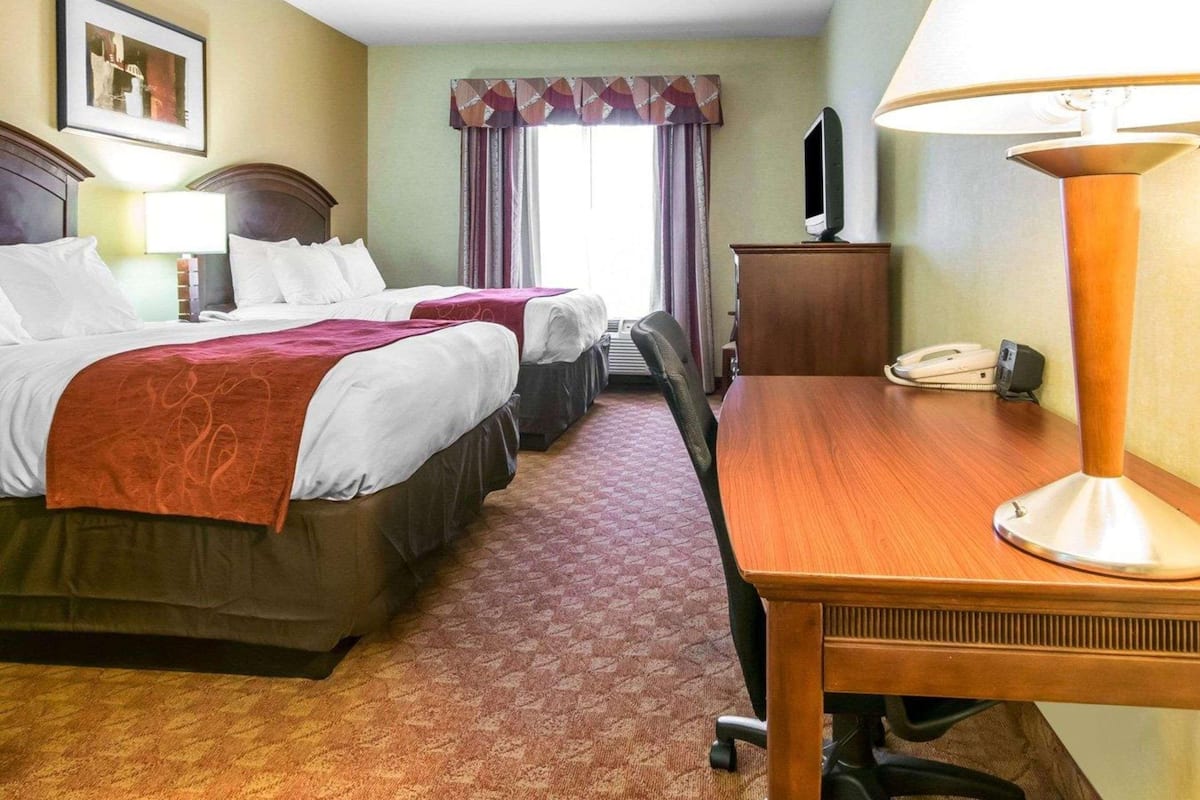 A hotel room with two beds, a desk, a chair, a lamp, a TV, and a telephone.