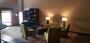 A hotel lobby with a sofa, armchairs, a bookshelf, and two lamps. - Comfort Suites South Point - Huntington (South Point)