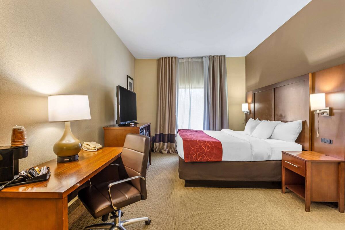 A hotel room with a bed, desk, chair, TV, and a window with curtains.