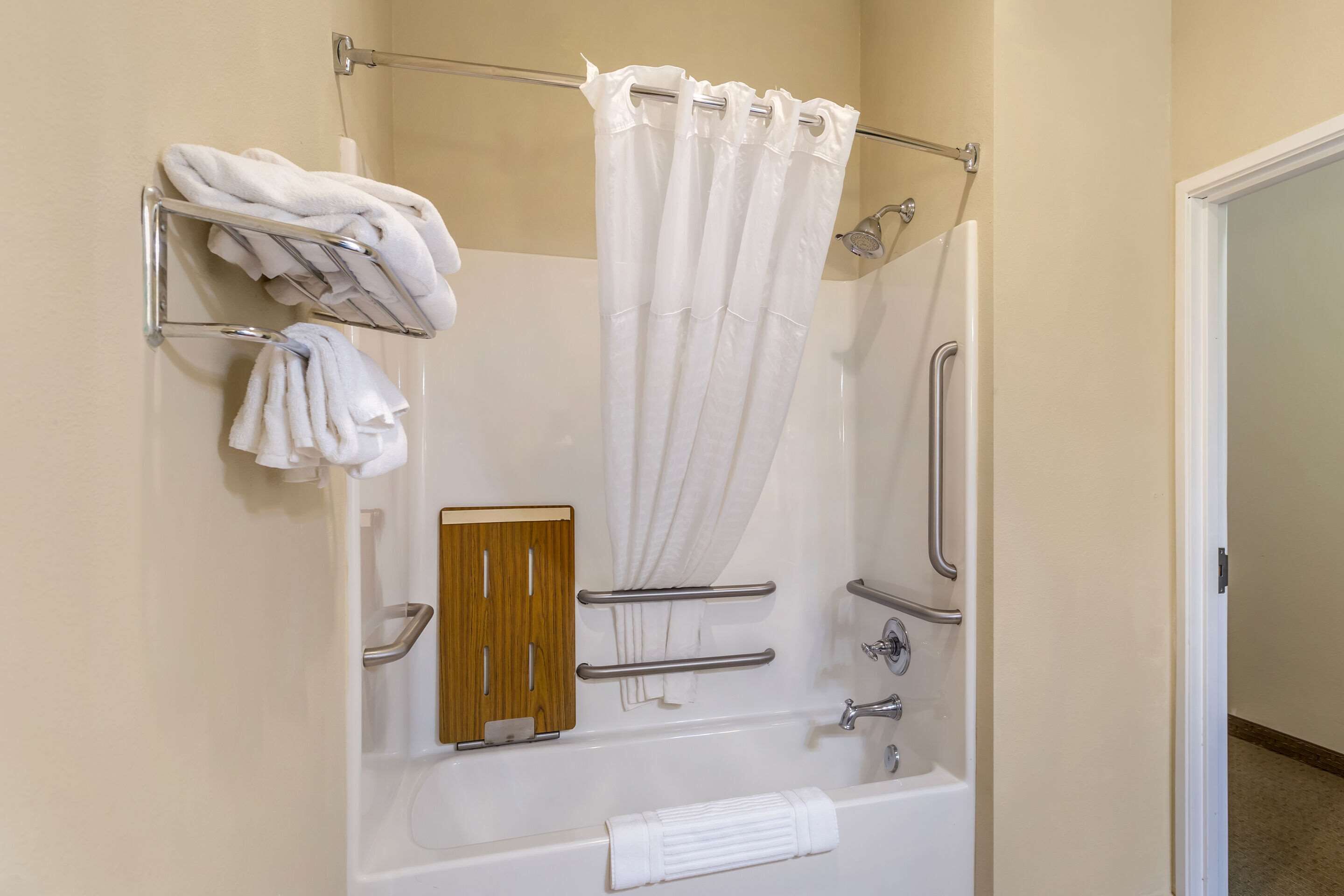 A modern bathroom with a bathtub, shower, and handrails.