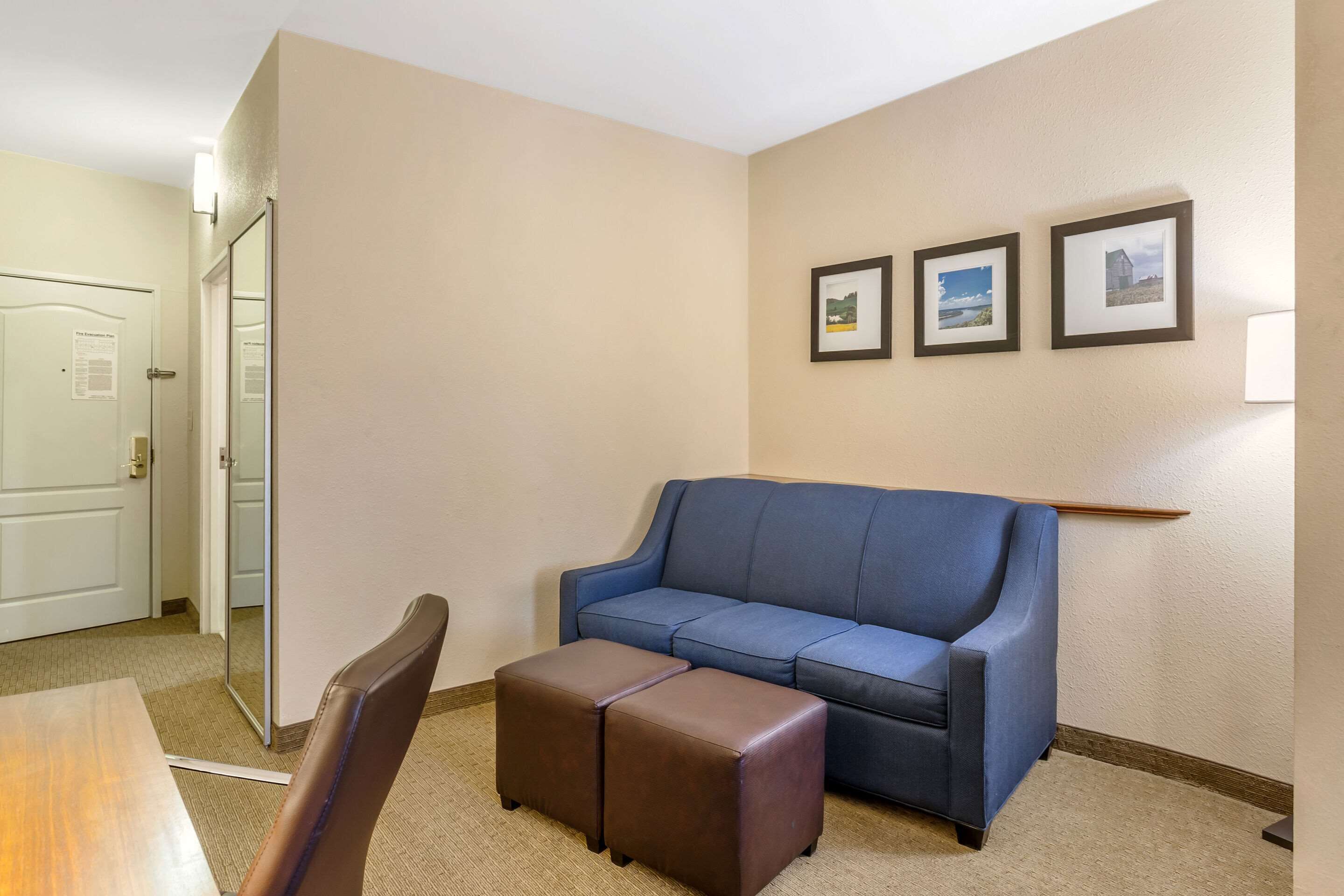 A room with a blue sofa, a wooden table, and a brown ottoman. There are three framed pictures on the wall.