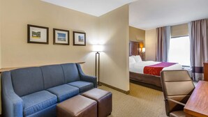 A hotel room with a blue sofa, a wooden table, a bed with a red blanket, and three framed pictures on the wall. - Comfort Suites South Point - Huntington (South Point)