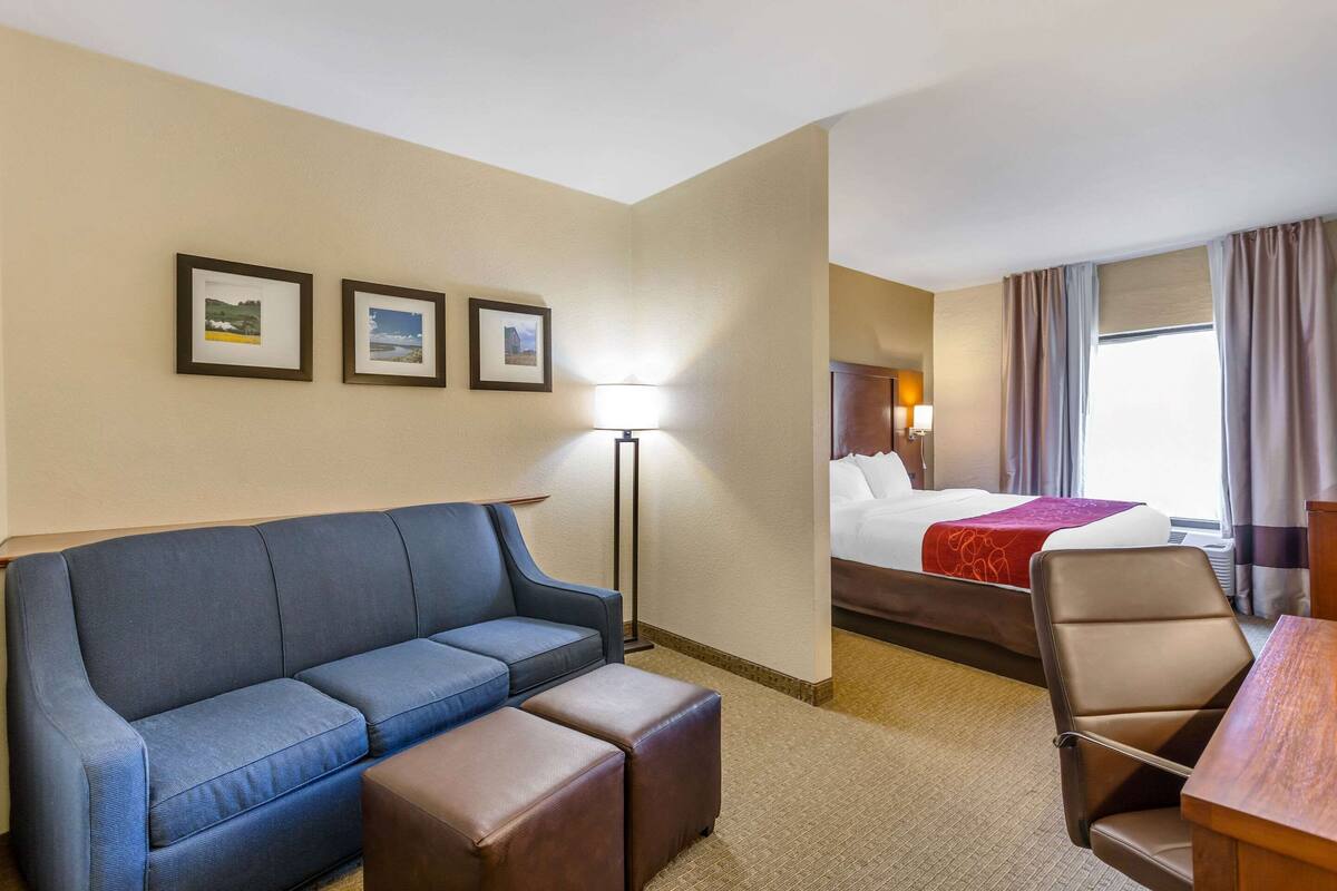 A hotel room with a blue sofa, a wooden table, a bed with a red blanket, and three framed pictures on the wall.