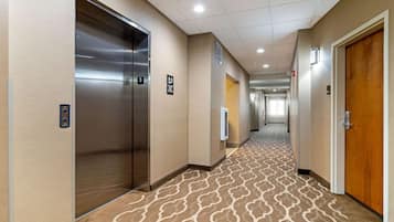 Un pasillo de hotel con un ascensor, una alfombra estampada y una puerta a la derecha.