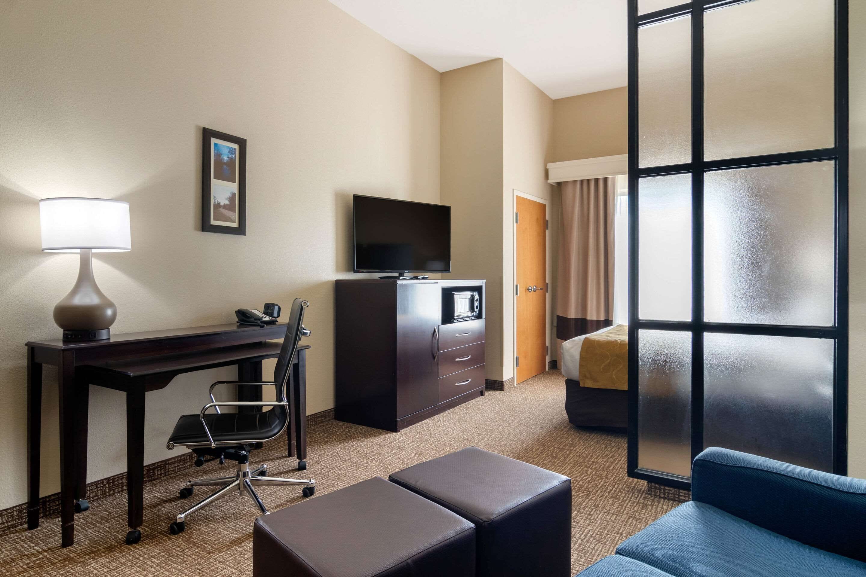 A hotel room with a desk, chair, TV, minibar, and a large window with a view.